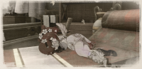 One of the small red-haired girls lays on a chaise lounge, sleeping and holding a doll that looks similar to her.